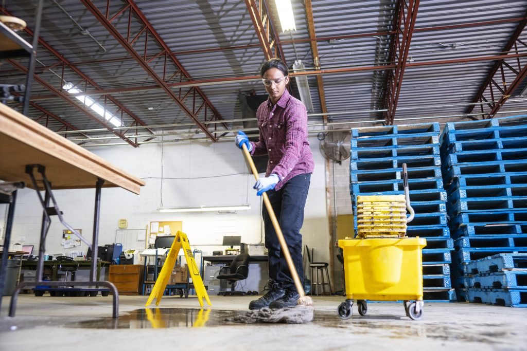 a worker in a warehouse cleaning up a hazard of spilled liquid.
