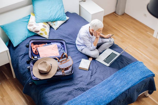 mature woman packing her suitcase and using a laptop.